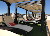 Thumbnail 25 of 25 - A row of sun loungers are arranged on a green carpet under a striped awning at The Olivia Apartments, Carmel, IN, 46032
