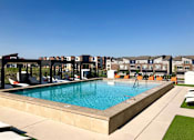 Thumbnail 12 of 25 - A swimming pool surrounded by lounge chairs and apartment buildings in the background at The Olivia Apartments, Indiana, 46032