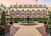 Thumbnail 5 of 35 - A courtyard with a fountain surrounded by flower pots and buildings in the background.