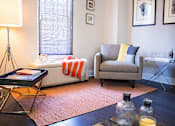 Thumbnail 1 of 7 - A living room with a grey couch, a coffee table, and a lamp.