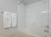 Thumbnail 18 of 35 - A white tiled bathroom with a white tub and towel racks at The Promenade at Easton Apartments, Easton