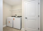 Thumbnail 19 of 35 - A white door is open to a room with two white washing machines at The Promenade at Easton Apartments, Maryland, 21601