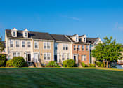 Thumbnail 21 of 50 - a row of houses on a green lawn with a blue sky at Townes at Village Center Apartments, Reisterstown, 21136