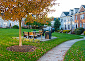 Thumbnail 39 of 50 - a park with a bench and a tree in front of houses at Townes at Village Center Apartments, Reisterstown, Maryland