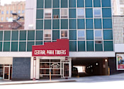 Thumbnail 4 of 14 - The Central Park Towers building is a large, modern structure with a red and white sign on the front.