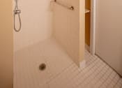 Thumbnail 11 of 14 - A white tiled bathroom with a shower and a door.
