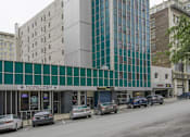 Thumbnail 5 of 14 - A modern building with a glass facade is situated on a street with cars parked in front.
