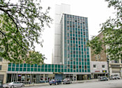 Thumbnail 6 of 14 - A tall building with many windows is in the middle of a street.