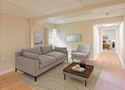 Thumbnail 13 of 14 - A living room with a grey couch, a white chair, and a coffee table.