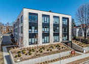 Thumbnail 4 of 19 - A modern building with a grey and black facade and a small garden in front.