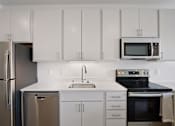 Thumbnail 12 of 19 - A modern kitchen with white cabinets and stainless steel appliances.