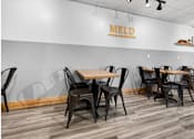 Thumbnail 32 of 52 - A dining area with chairs and tables in front of a wall with the word MELD on it.