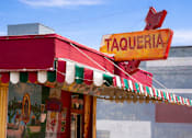 Thumbnail 58 of 64 - A red and yellow taqueria with a red bench in front.