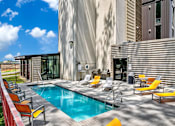 Thumbnail 3 of 50 - A pool with yellow chairs and a building in the background.