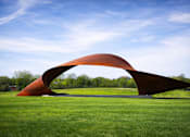Thumbnail 59 of 64 - A large, curved, orange sculpture sits in a grassy field.