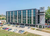 Thumbnail 6 of 50 - A modern building with a glass facade and a parking lot in front.