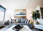 Thumbnail 12 of 22 - A living room with a grey couch, a painting on the wall, and a coffee table with a black box on it at Cityplace Apartment Homes Apartments, Pennsylvania