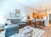 Thumbnail 7 of 26 - A grey sofa with a white pillow is in the middle of a room with a wooden table and chairs at The Hive Apartments, Allentown
