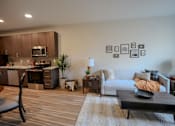Thumbnail 4 of 15 - A modern living room with a couch, coffee table, and kitchen area.