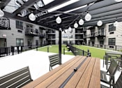 Thumbnail 18 of 22 - A wooden table is in the foreground of a patio with chairs and a view of apartment buildings.