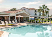 Thumbnail 29 of 58 - A pool area with sun loungers and a building in the background.