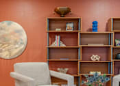 Thumbnail 49 of 58 - A living room with a chair, a table, and a shelf with various objects.