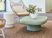 Thumbnail 23 of 58 - A white chair with a woven back is placed on a green table with a white vase of flowers on it.
