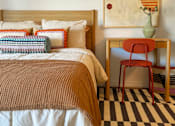Thumbnail 1 of 16 - A bed with a brown blanket and a red chair in front of a painting at The Teale Siesta Lago in Kissimmee, FL, 34746