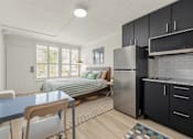 Thumbnail 15 of 20 - A kitchen with a refrigerator, a dining table with chairs, and a bed with a striped comforter.