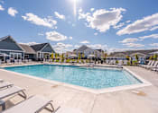 Thumbnail 10 of 31 - A large outdoor swimming pool surrounded by sun loungers and a building in the background.