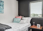 Thumbnail 7 of 25 - A bedroom with a bed, pillows, a blanket, and a small table with a sign on it.