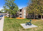 Thumbnail 28 of 34 - A green picnic table sits in the middle of a grassy area in front of a building.