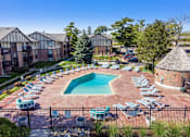 Thumbnail 11 of 25 - A pool surrounded by chairs and trees in front of apartment buildings.