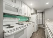 Thumbnail 22 of 34 - A white kitchen with a stove top oven and a microwave above it.
