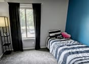 Thumbnail 5 of 34 - A bedroom with a striped bedspread and a window with curtains.
