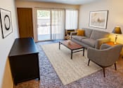 Thumbnail 3 of 20 - A living room with a grey couch, a brown chair, a brown coffee table, and a brown cabinet.