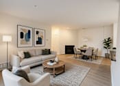 Thumbnail 4 of 38 - A living room with a grey sofa, a grey armchair, a wooden coffee table, a grey rug, a black fireplace, a dining table with chairs, and two framed artworks on the wall.