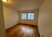 Thumbnail 3 of 7 - An empty living room with wooden floors and two windows