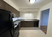 Thumbnail 4 of 7 - An empty kitchen with black appliances and wooden cabinets