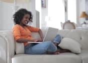 Thumbnail 9 of 36 - Woman relaxing on couch at Living room at Southfield MI Apartments | 42 West Apartments in Southfield Michigan