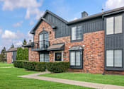Thumbnail 23 of 26 - A red brick house with a balcony and a green lawn in front.