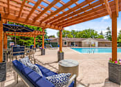 Thumbnail 19 of 33 - A wooden pergola over a pool area with a blue lounger.