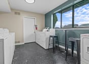 Thumbnail 18 of 21 - a laundry room with washing machines and a counter with two stools  at Park On Canal Apartments, Clinton Twp, MI
