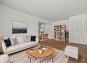 Thumbnail 3 of 26 - A living room with a white couch, a coffee table, and a bookshelf.