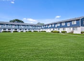 Thumbnail 13 of 14 - A large grassy area in front of a building with a tree.