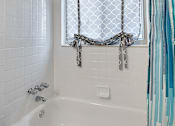 Thumbnail 23 of 28 - A white bathtub with a shower curtain tied in a bow.
