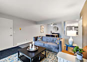 Thumbnail 17 of 28 - A living room with a grey couch, a black coffee table, and a blue side table.