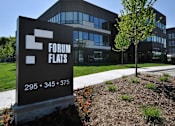Thumbnail 29 of 38 - A sign for Forum Flats stands in front of a modern building.