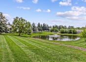 Thumbnail 82 of 87 - A serene landscape with a pond, trees, and a clear sky.
