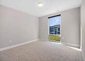 Thumbnail 32 of 38 - A room with a carpet floor and a window showing a view of a building.